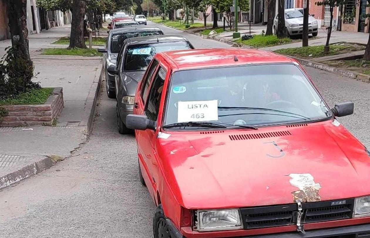 Cola de autos de distintos acoples que llevan a personas a votar, con el número identificatorio de su respectiva lista